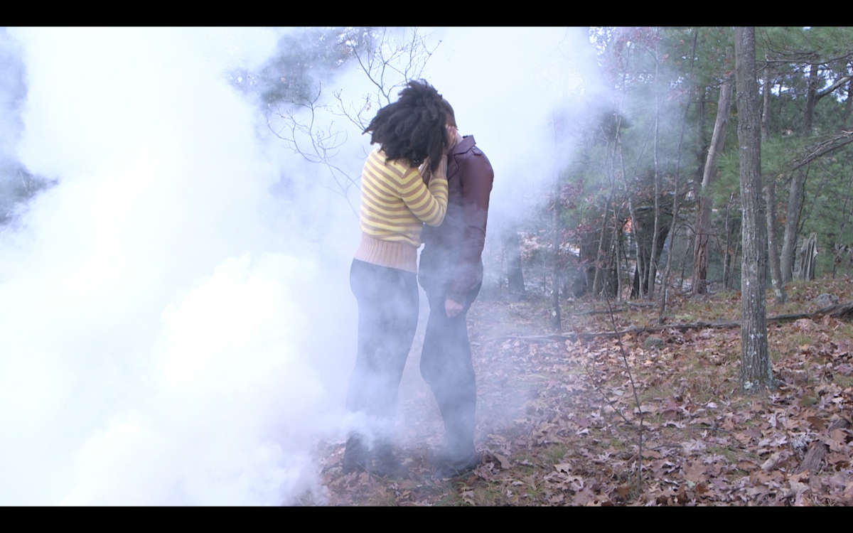 Two young people kiss in a cloud of smoke in the woods.
