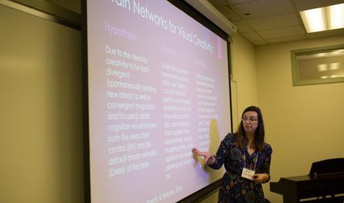 Woman in front of screen presenting on brain networks for creativity