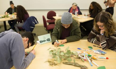 Participants sit at tables working with markers and natural materials