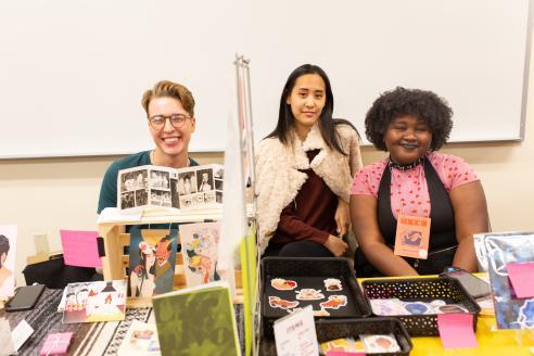 Three students behind a table at a comic book convention