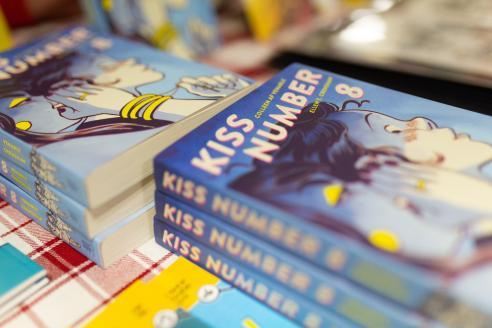 Photograph of a table of comic books and graphic novels stacked on each other