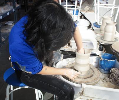 students works at a potter's wheel making a clay vase
