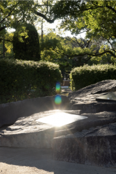 Light seen reflecting through trees shining and reflecting onto a plaque built into a large stone in the Hiroshima Peace Memorial Park.