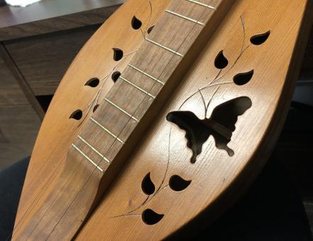 Close-up of a wooden dulcimer with cutouts of ivy and a butterfly.