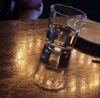 A half-full glass of water on a wooden table encircled by the reflection of above lighting.