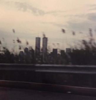 Blurry image of the side of the road. The twin towers and the New York City skyline can be seen in the distance.