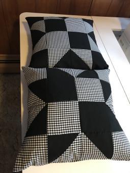 Two sewn pillowcases with 8-point star pattern with black and white/black buffalo plaid fabric laying on a white table. Dimensions 16 inches by 16 inches.