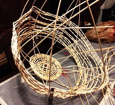 Progress photograph of the artist's Nest sculpture forming with reeds woven together to form the start of a sphere. 