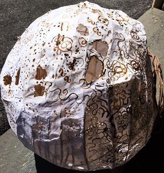 Large spherical sculpture constructed from reed and white rice paper. There are holes exposing the inside of the structure. On the outside, are brown ink drawings of swirls and lines.