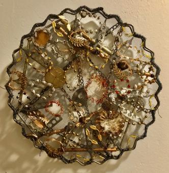 Circular mesh metal shape with wavy edges. Metal and mesh is silver and bronze. Affixed atop the mesh screen are varying gold, copper, black, silver, and red beads and wire creating layered objects.