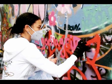 Student wearing a mask spray painting a wall