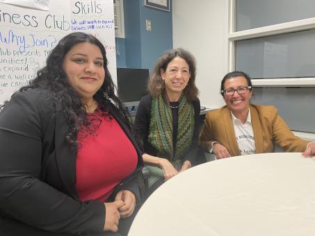 The two speakers and the business club faculty member sitting at a table in front of a white board