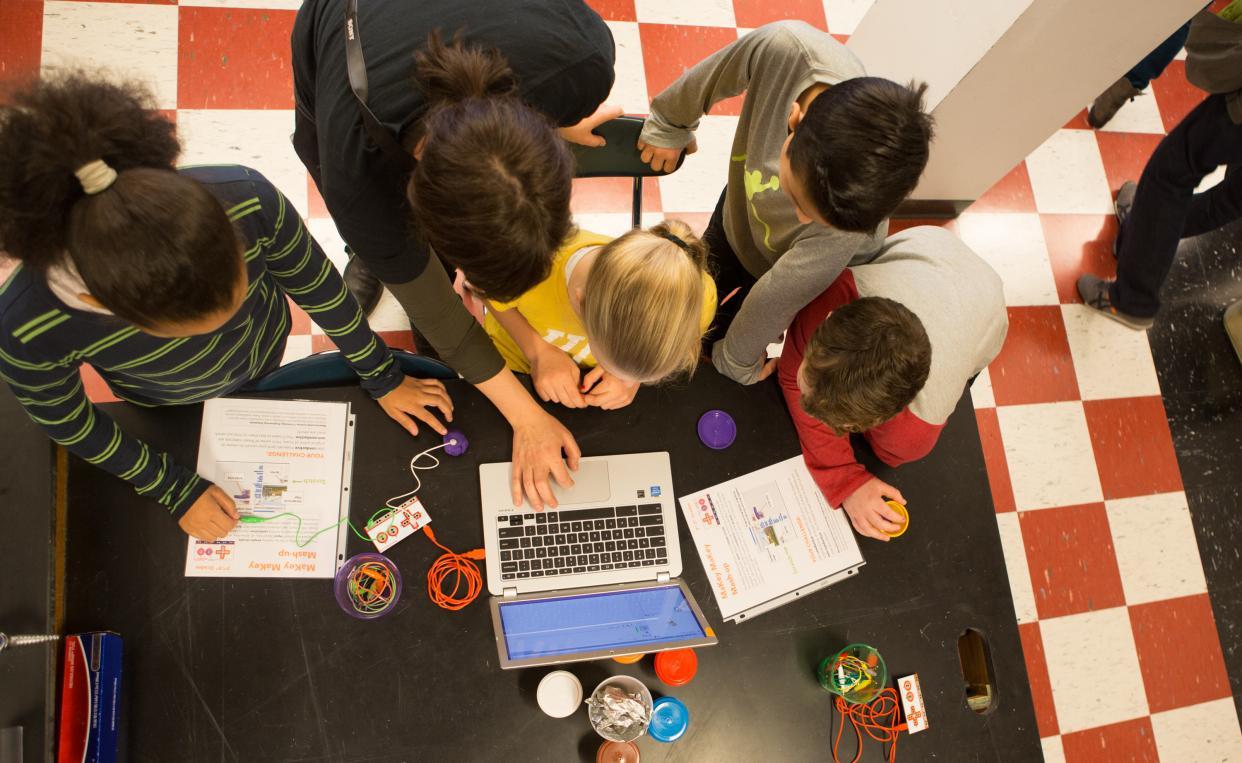 Students and a teacher crowding around a computer and circuit boards, finalizing their coding project