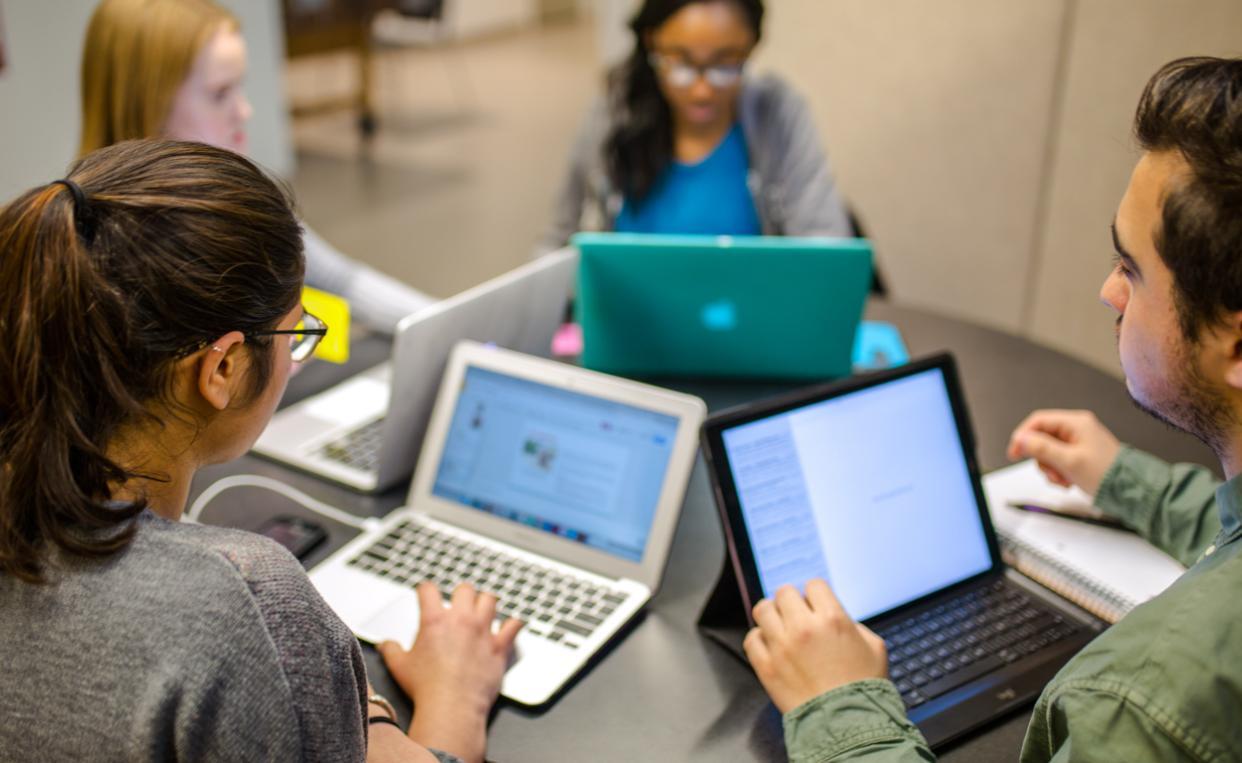 A group of students work on laptops at a table. 