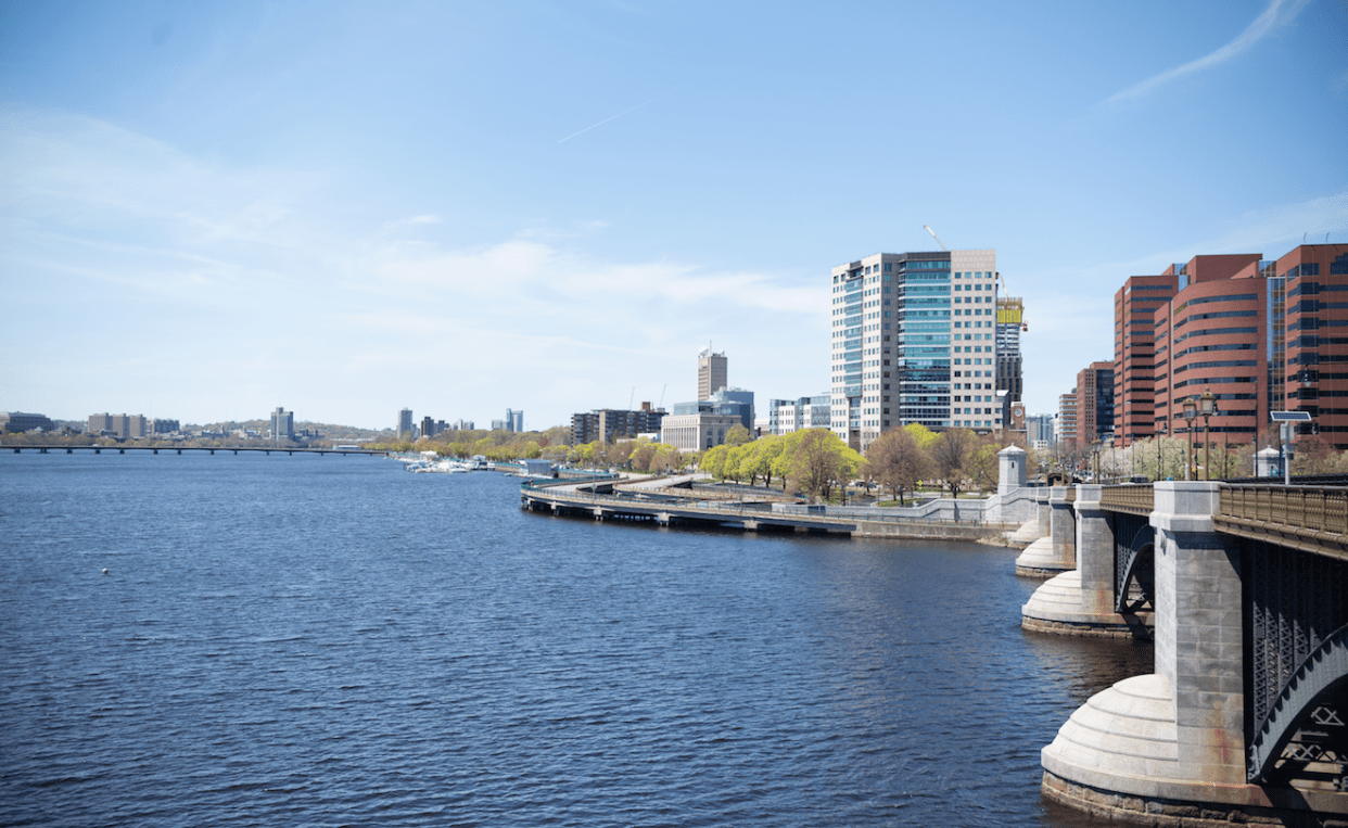 Photograph of the Charles River with blue sky and blue water and buildings of Cambridge in the background.