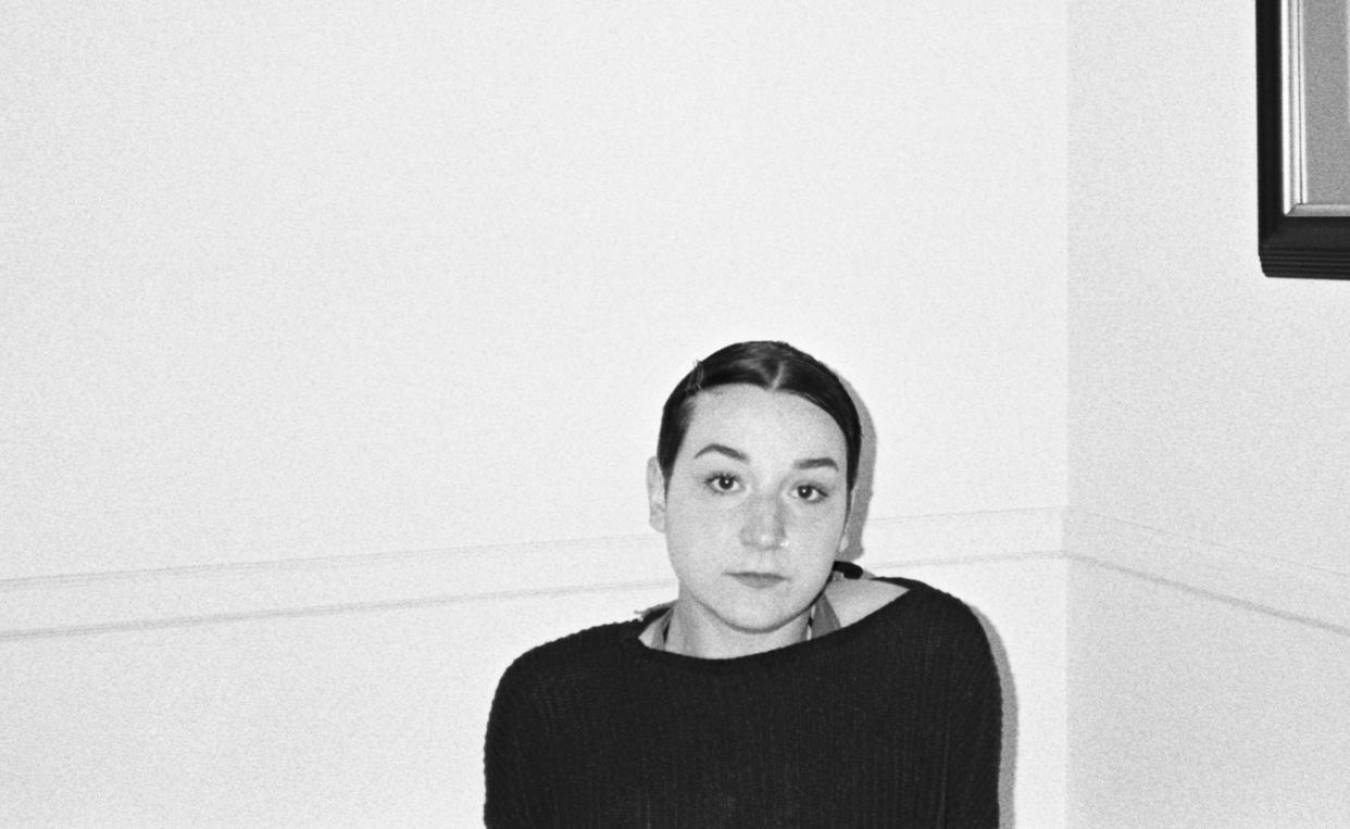 black and white photo of young woman sitting in empty white room wearing a black sweatshirt