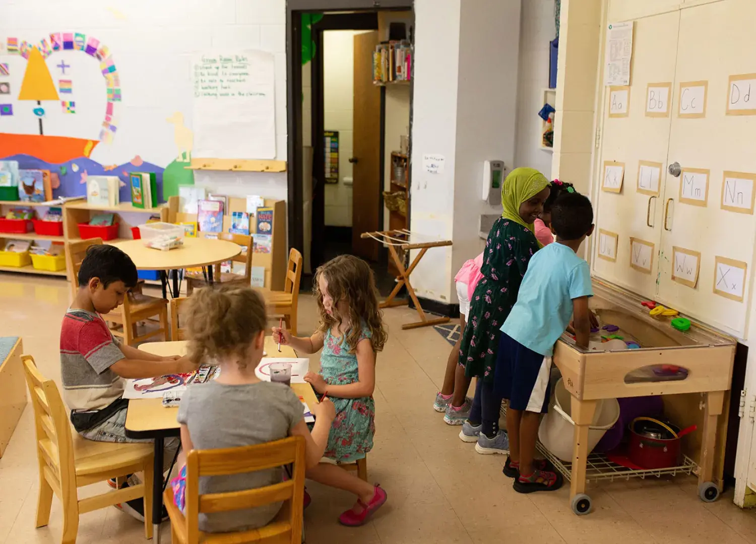 Young children paint and play at a sensory table in a classroom