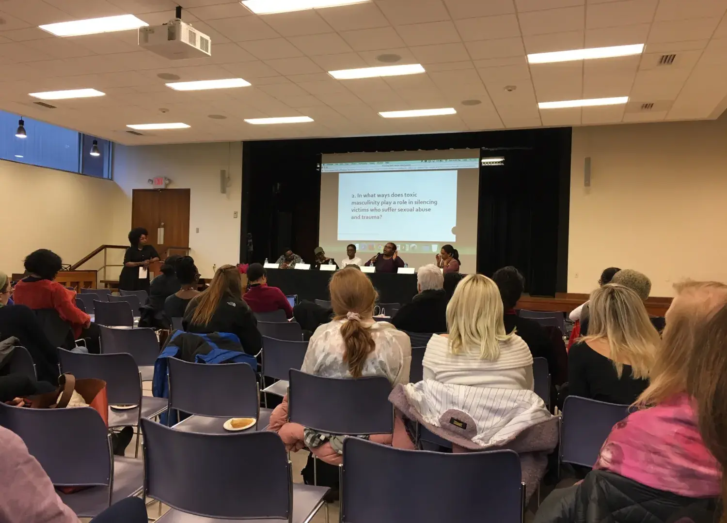 View from rear of the room of the panelists, audience and powerpoint slide.