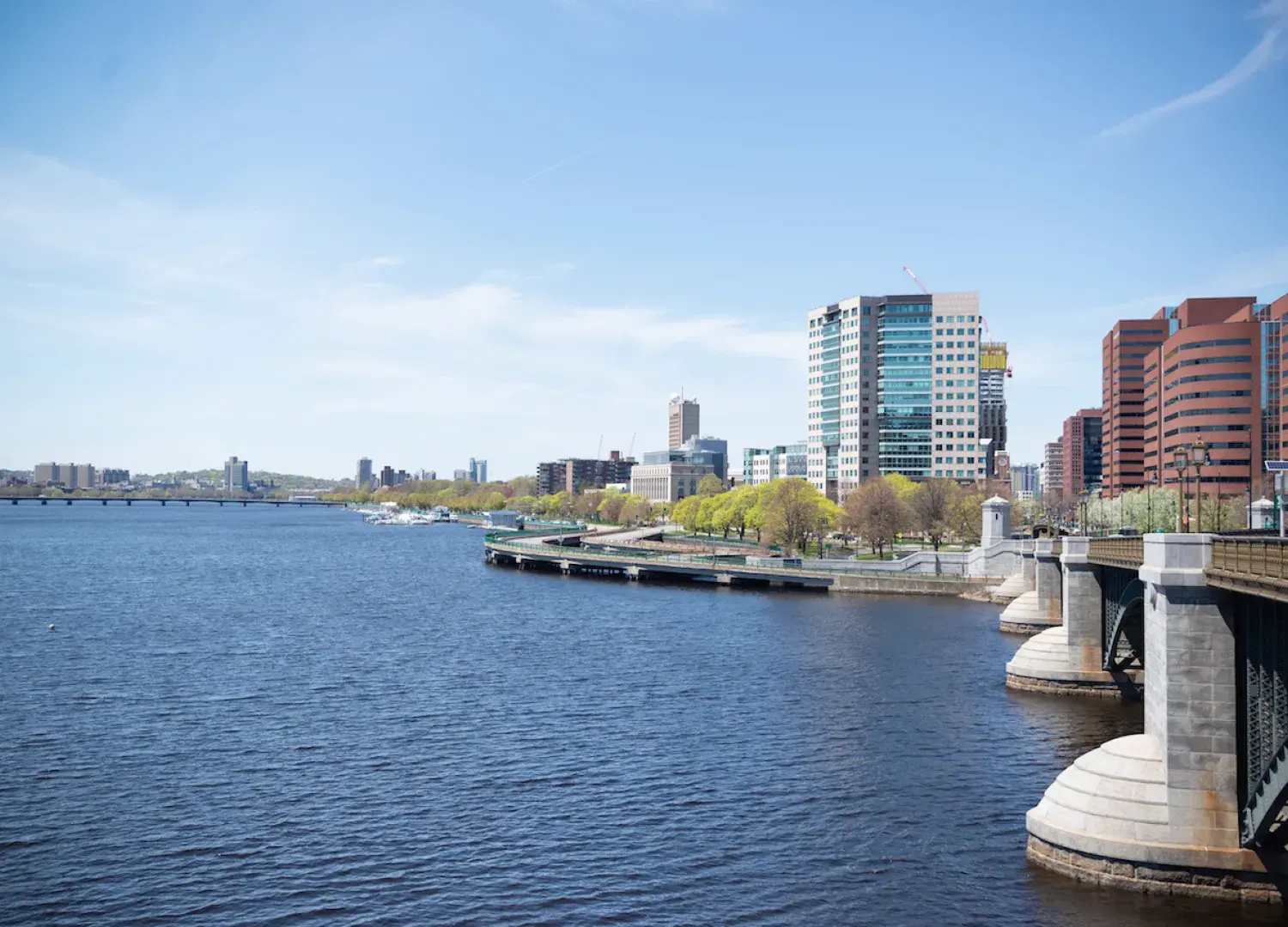 Photograph of the Charles River with blue sky and blue water and buildings of Cambridge in the background.