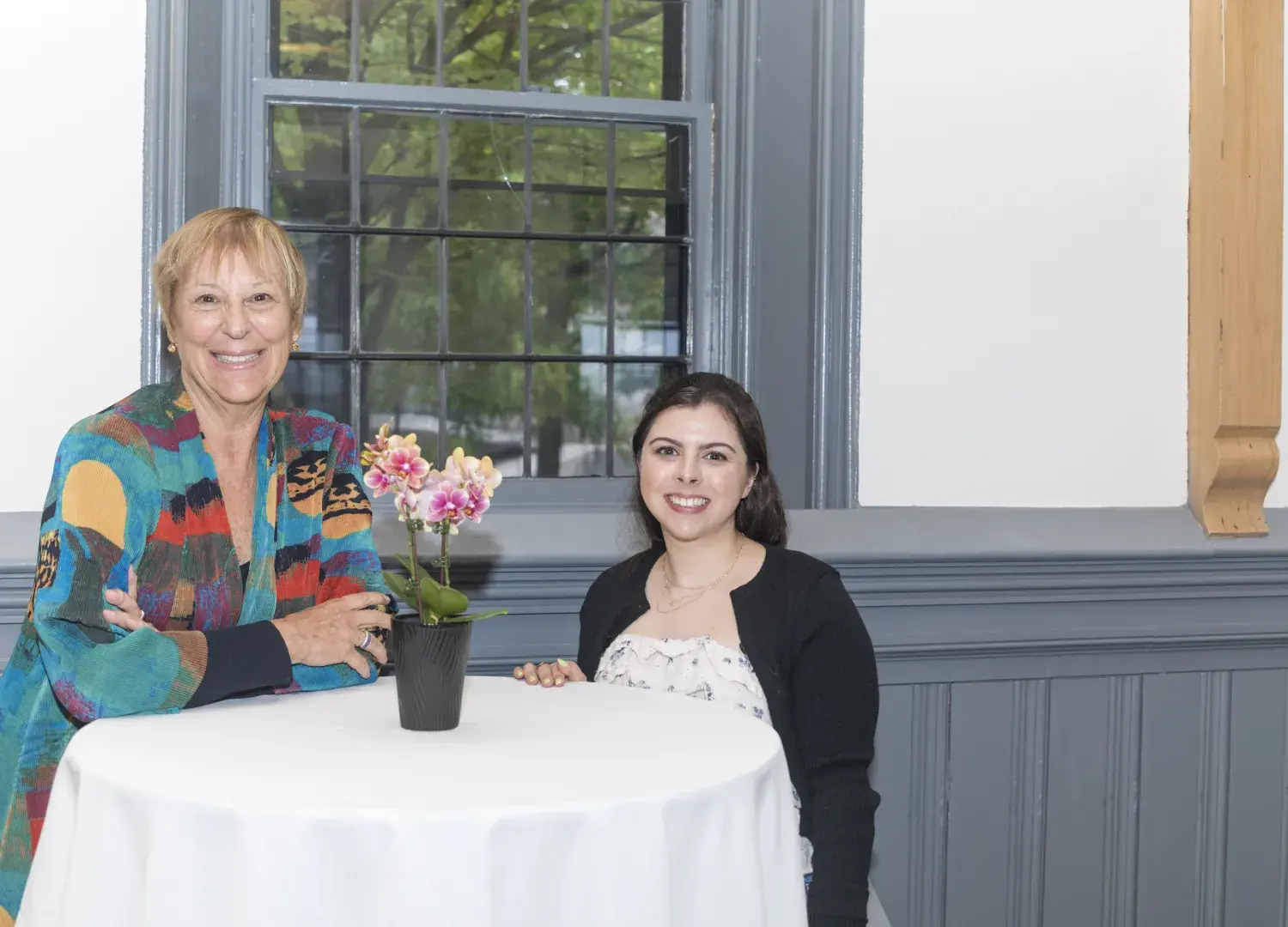 two women standing in front of round white table with flowers