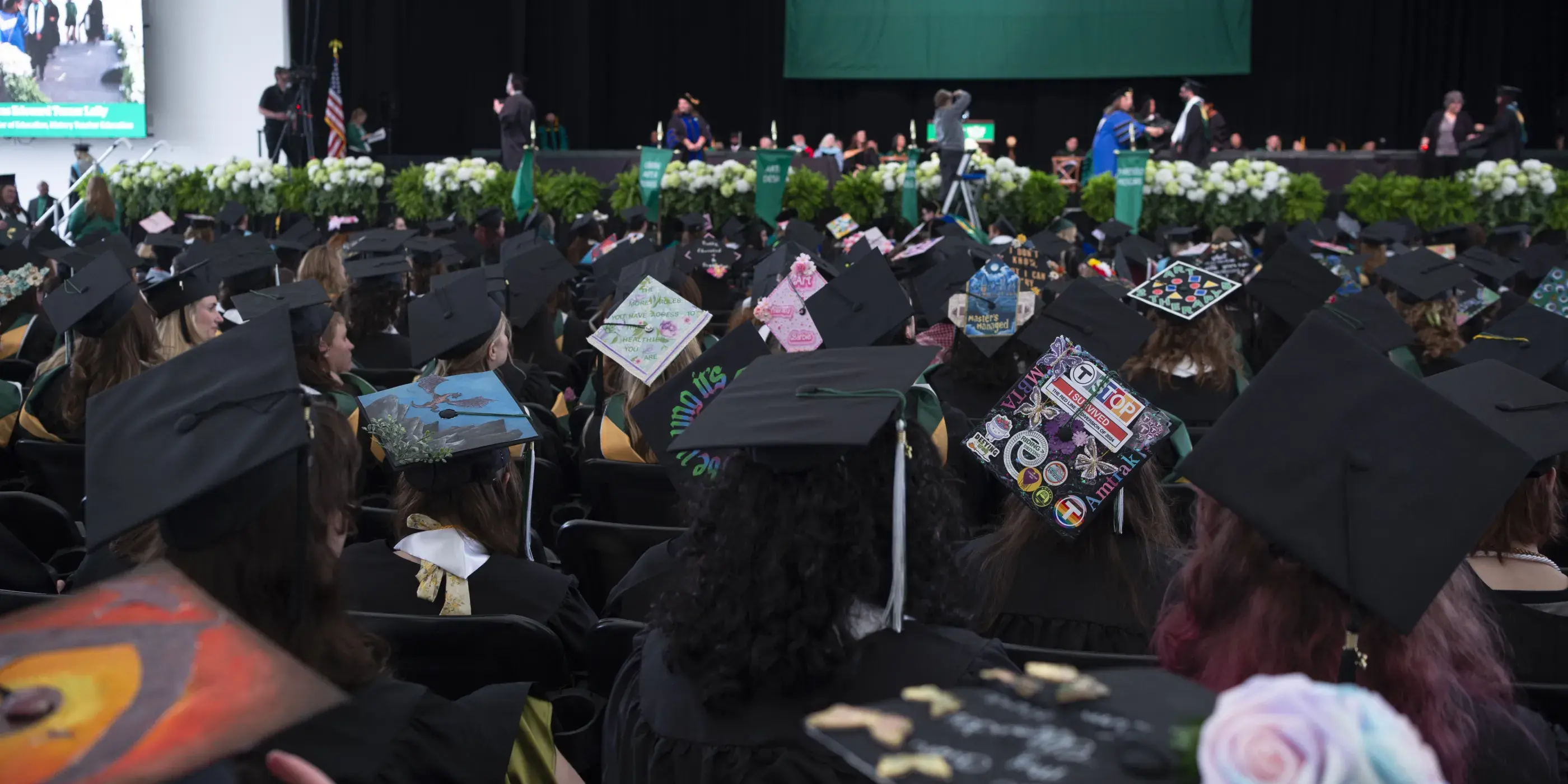 Graduates seated facing stage with Lesley banner