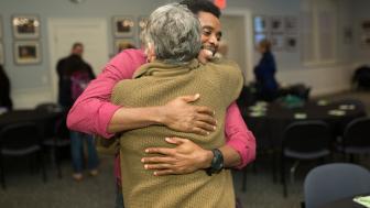 Student Lesly Precil in a pink shirt hugs professor Jan Wall in a mustard sweater.