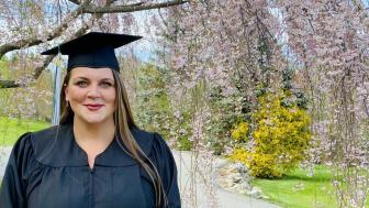 Alice Smith in graduation gown outside in front of blooming tree.