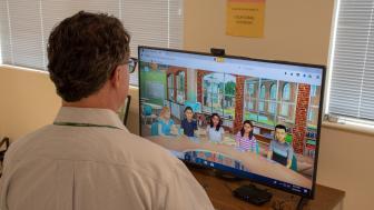 A man looks at a wide screen TV where the images of avatars are displayed.