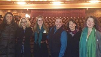 group of six people standing on stage in front of empty auditorium