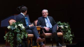 two men sitting on a stage in conversation for an interview