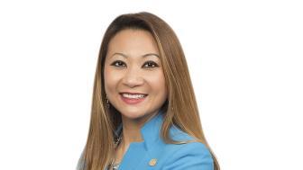 New trustee member Bopha Malone stands with her arms crossed in a blue suit.