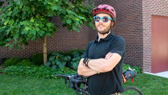 Brendan Walsh wearing his helmet and sunglasses, standing with arms crossed in front of bike.