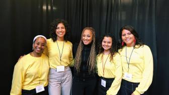Four volunteers in yellow T-shirts flank actress Amanda Seales, dressed in all black
