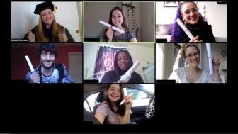 Screenshot of a Zoom call, students hold up paper rolled up to look like diplomas. Professor Eisenbach wears her regalia.