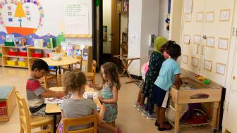 Young children paint and play at a sensory table in a classroom