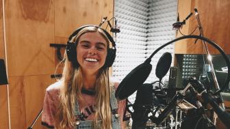 Carly Eaton in a music studio with headphones on standing in front of a mic