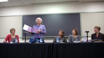 Evelyn Finnegan in 2011 holding a picture book and standing at a table with a panel of people