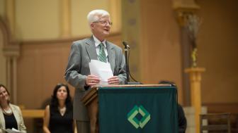 Interim President Hansen stands at a podium speaking into a microphone