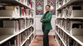 Gloria Noronha standing among the stacks in the library