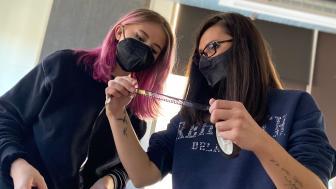 Two people wearing masks examine a film reel.