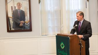 Joe Moore speaks at a podium in Alumni Hall in the foreground of his portrait