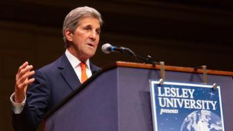 John Kerry speaks in front of a podium while gesturing with his right hand