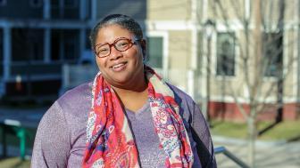 Kenish Coy poses in the sunshine on the Quad in a purple shirt and red-and-white scarf