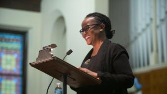 Woman standing at podium talking into microphone with a big smile on her face