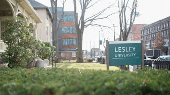 Photograph of admissions building shrubs and exterior with Lesley sign and sidewalk in the background.