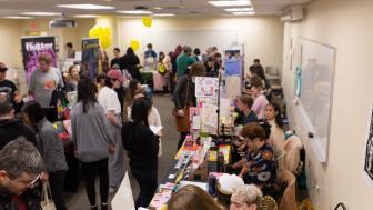 Crowd at a comic book festival inside of a classroom with tables and balloons