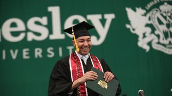 Young man walking across the stage with his diploma at Lesley Commencement in 2019.