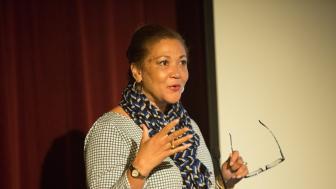Michele Norris speaks at a podium, holding a pair of glasses in her left hand.