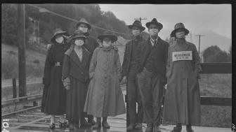 Black and white photo of women from 1918. one holding sign: Wear a mask or go to jail.