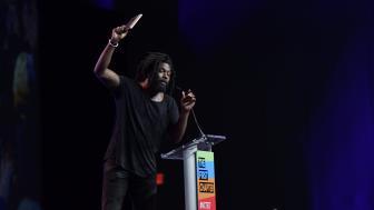 Author and creative writing faculty Jason Reynolds holds a book in the air as he speaks at the conference.